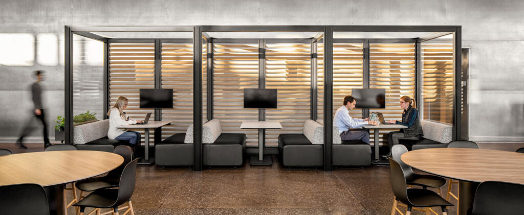 Modern workplace café with wood slat partitions, communal seating, pendant lights, and service counter