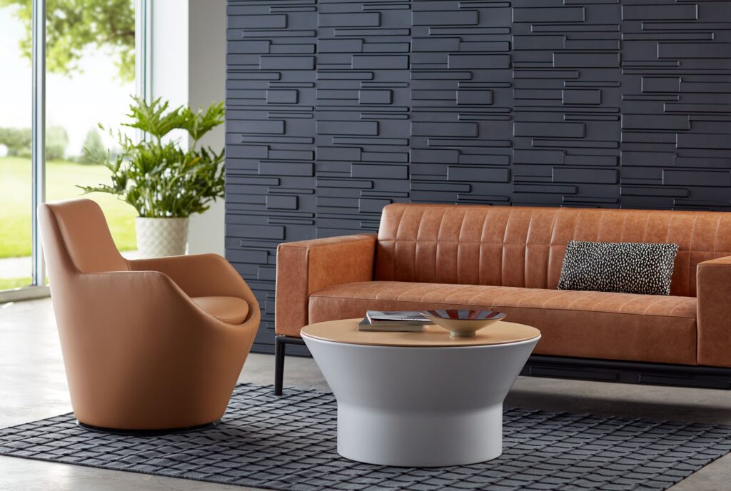 Contemporary office lounge with caramel leather sofa, round table, plants, and textured wall panels