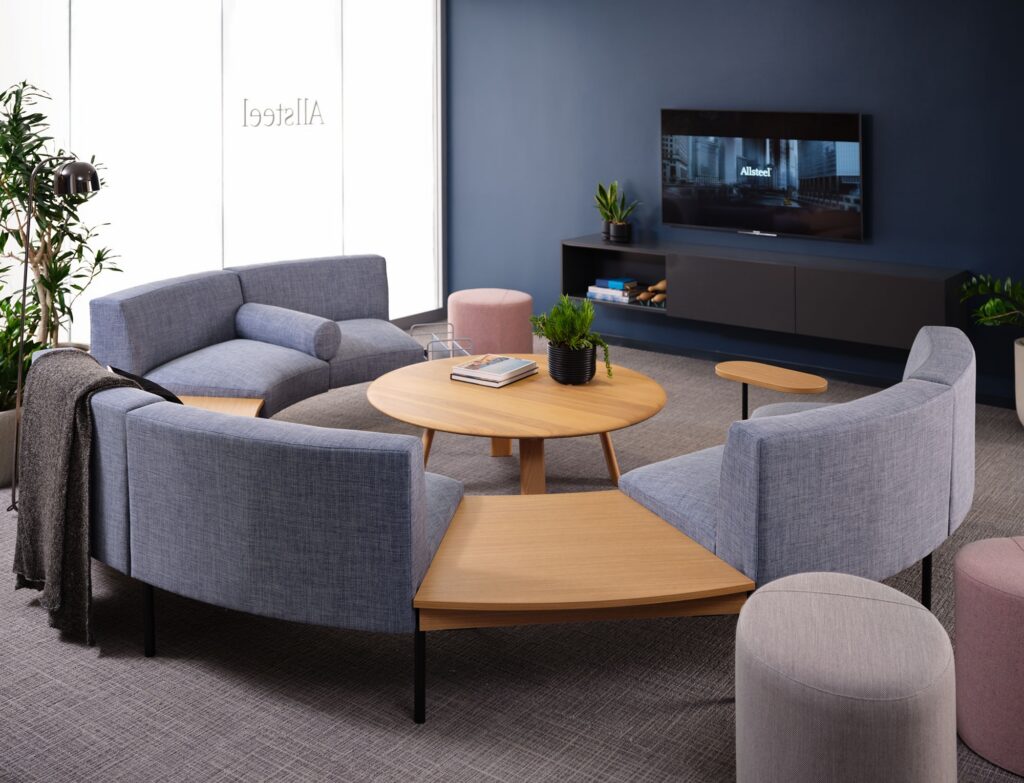 Collaborative office lounge with upholstered sofas, round tables, and wall-mounted display