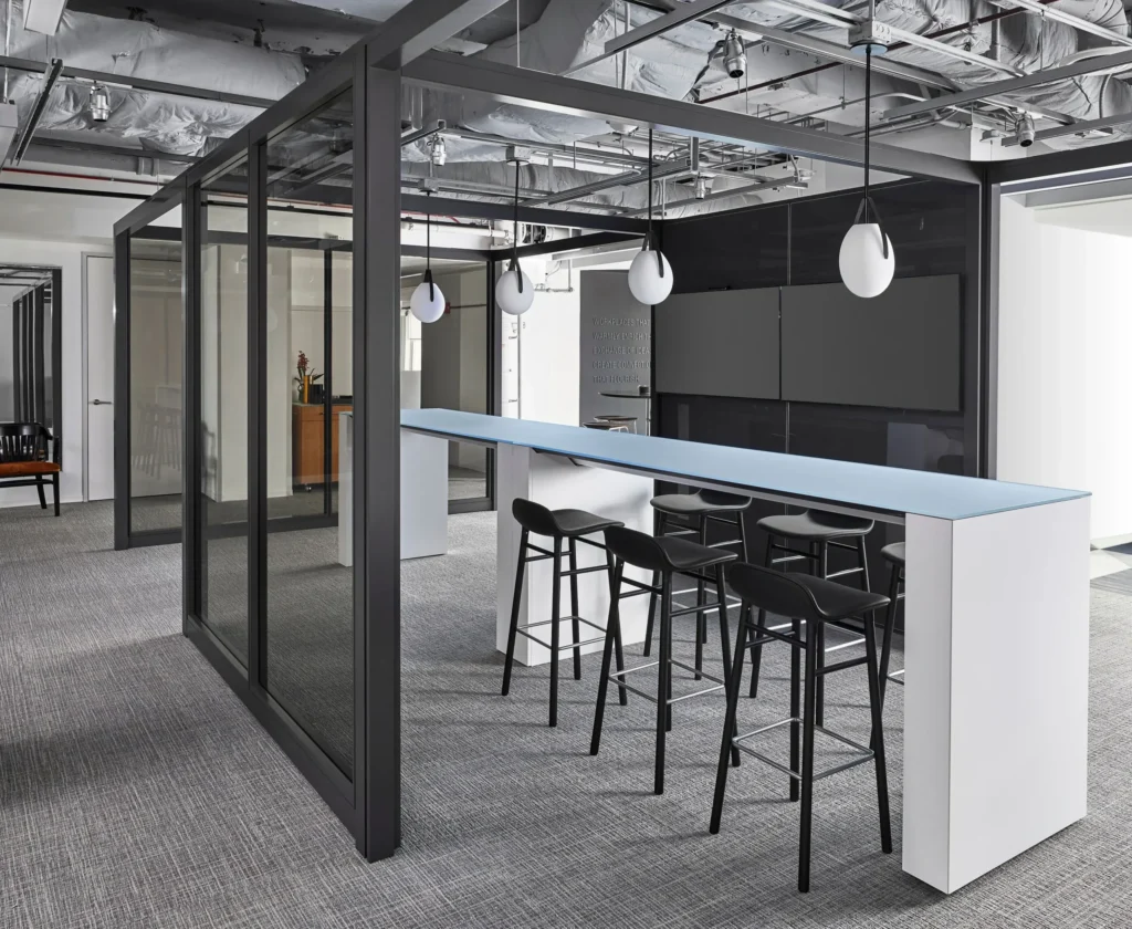 Glass-enclosed meeting room with black framing, wood ceiling details, and collaborative seating