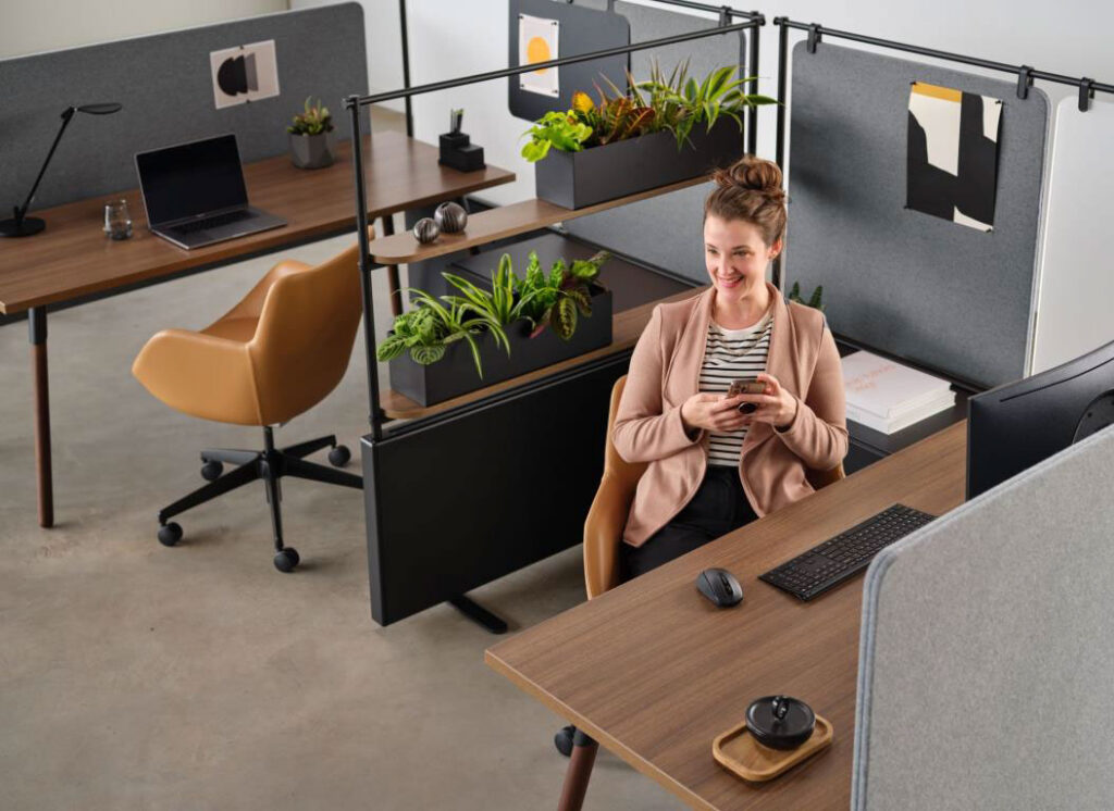 Employee seated at a modern workstation with planter dividers, task lighting, and office storage