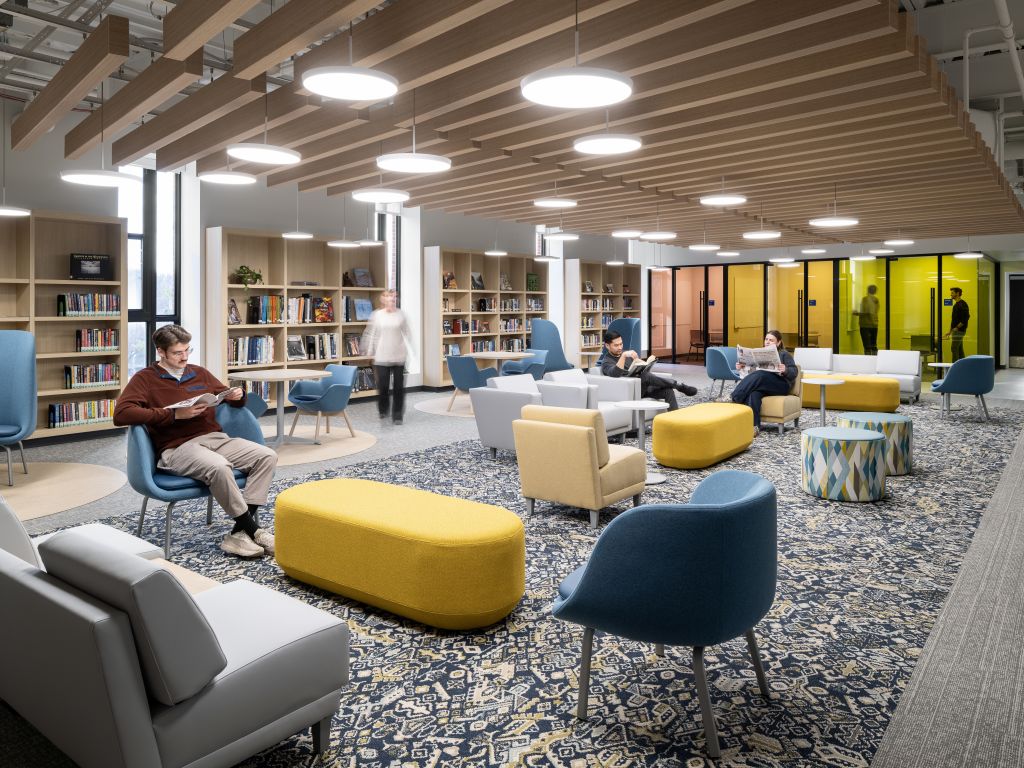 Open library with collaborative tables, colorful lounge seating, bookshelves, and wood ceiling panels