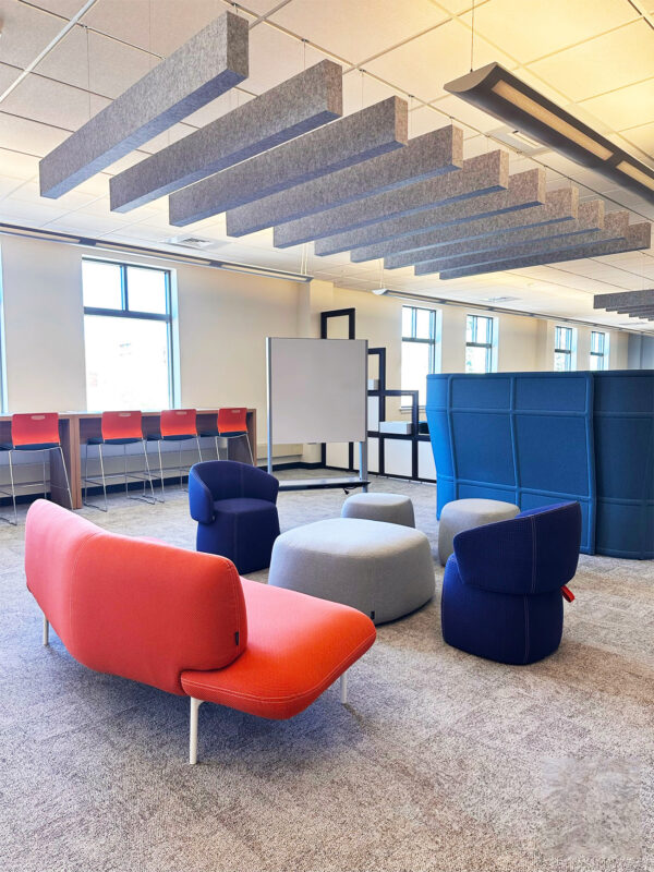 Collaborative lounge with blue and orange seating beneath suspended acoustic ceiling baffles