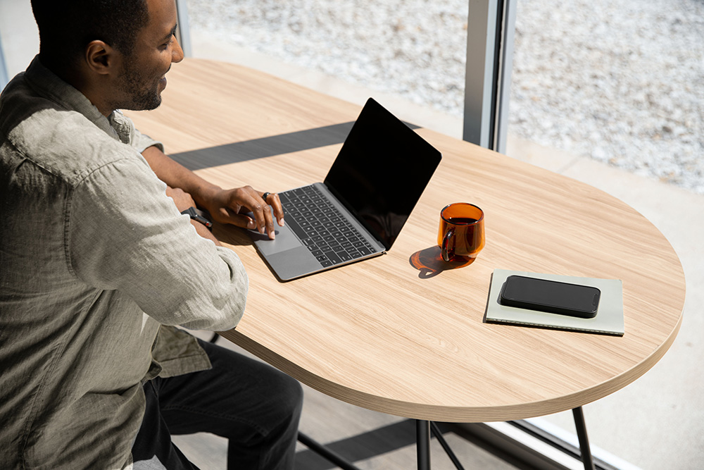 Employee working on a laptop at a light wood Picnic table in a bright collaborative space