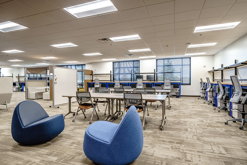 Healthcare training room with rows of tables, office chairs, presentation screens, and medical equipment