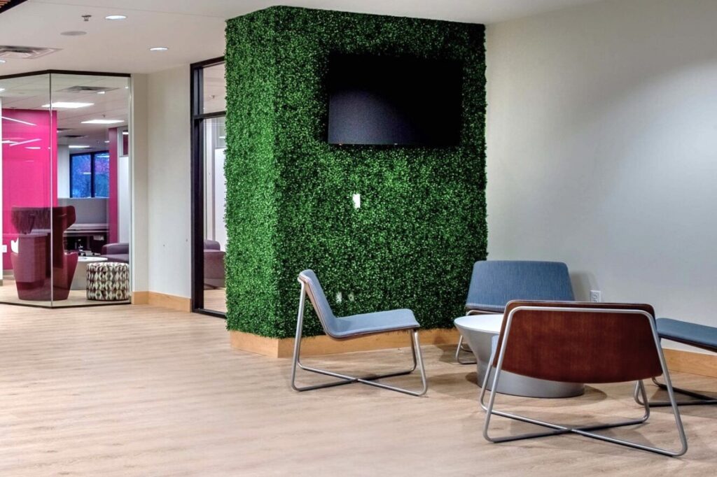 Green acoustic office pod with a mounted screen, lounge chair, and small table in a shared workspace