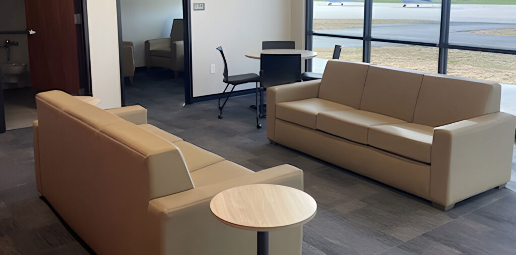 Healthcare waiting area with modular lounge seating, side tables, and glass office partitions