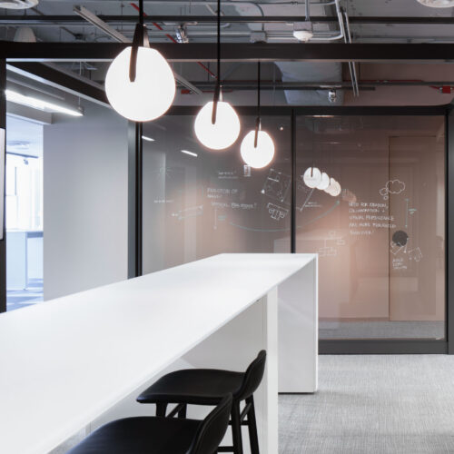 Glass office wall system beside a modern reception counter with suspended pendant lighting
