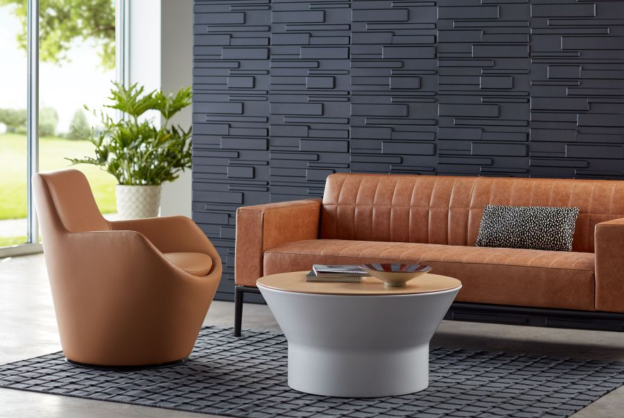 Contemporary office lounge with a caramel leather sofa, lounge chair, greenery, and textured wall