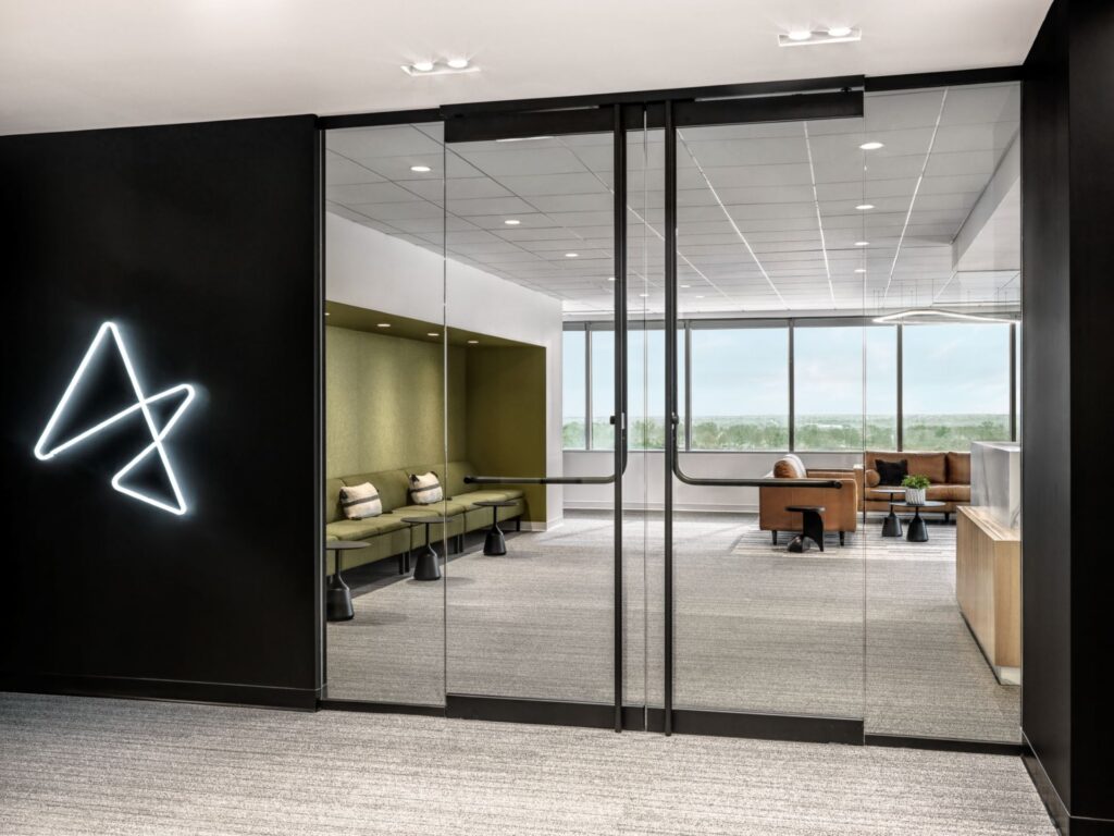 Glass-walled office entry leading to a contemporary reception and collaborative lounge area
