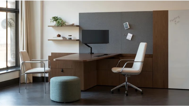 Modern private office with a wood desk, ergonomic chair, guest seating, monitor, wall storage, and writable panel.