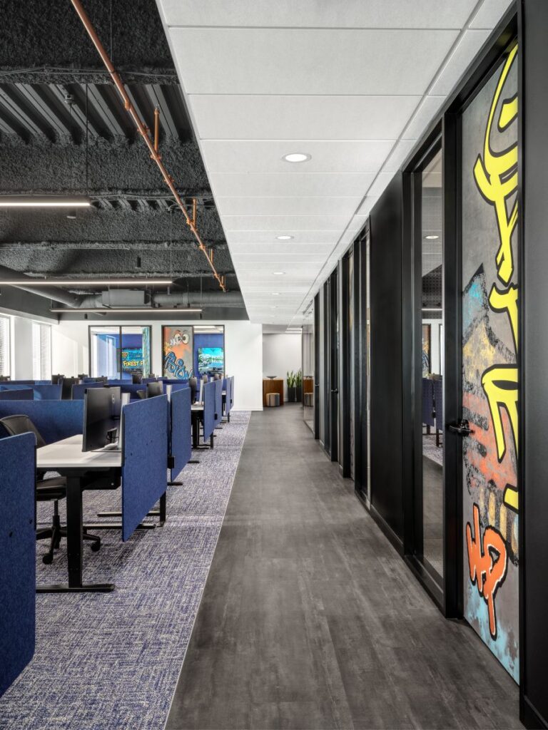 Open office with bench workstations, blue chairs, glass partitions, and exposed ceiling details