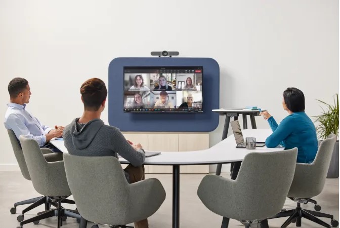 Modern conference room with three employees participating in a video meeting on a wall-mounted display.