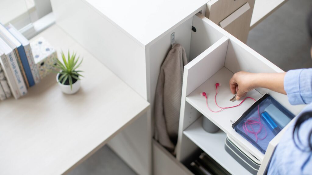 Employee placing keys into a personal storage locker with open shelving, a coat compartment, books, and office supplies.