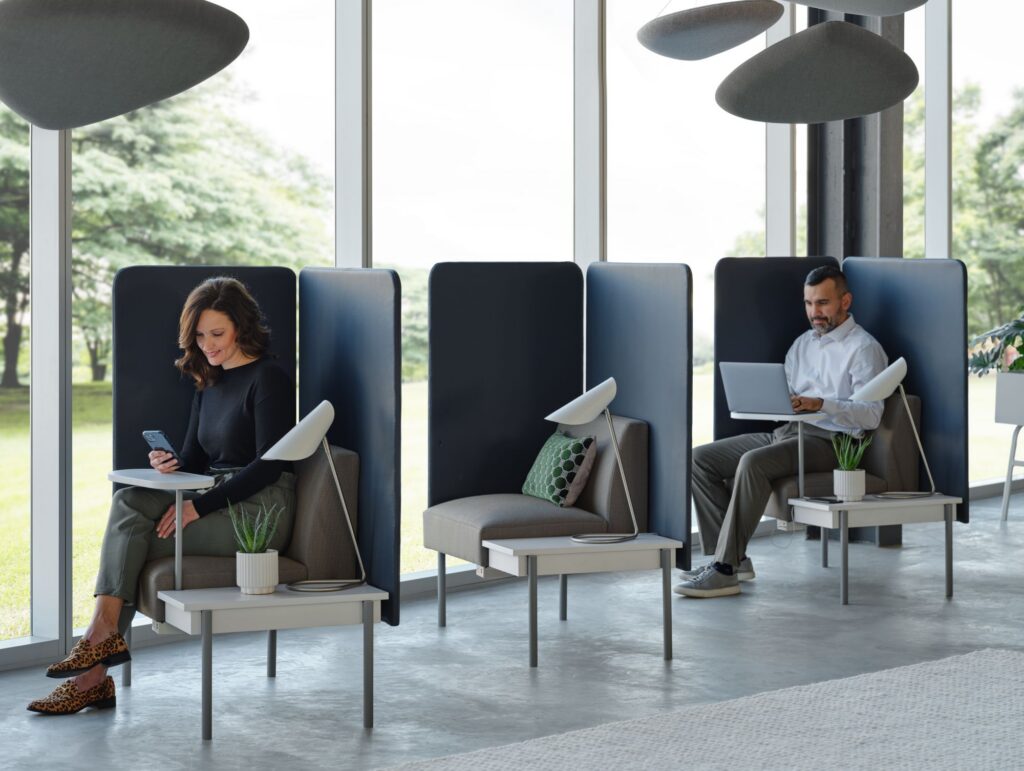 Two professionals using private high-back office lounge chairs with built-in tables, task lighting, and acoustic privacy panels.
