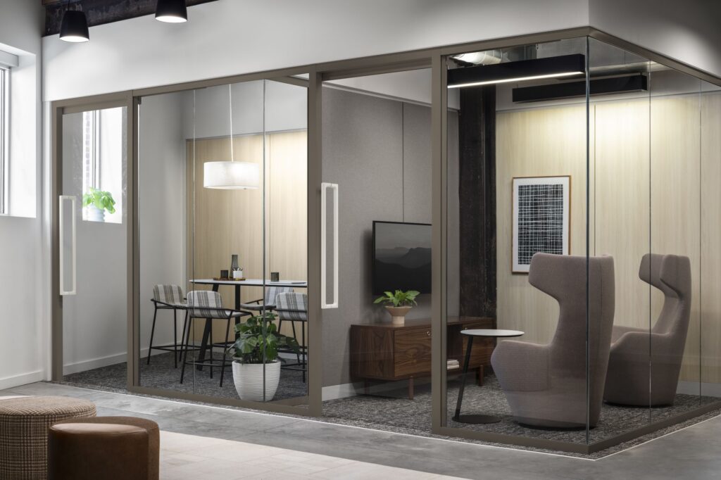 Glass-enclosed office suites with a small conference room, high-back lounge chairs, wood accents, and integrated lighting.