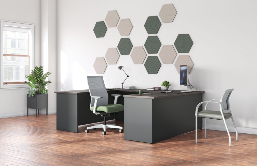 Modern private office with an L-shaped desk, ergonomic task chair, guest seating, computer monitor, and hexagonal acoustic wall panels.