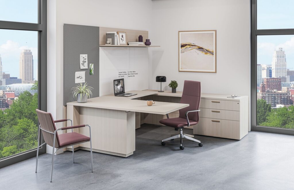 Modern executive office with an L-shaped desk, burgundy task chair, guest seating, built-in storage, and floor-to-ceiling city views.