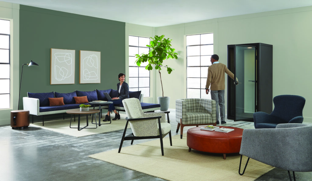 Modern office lounge with assorted seating, collaborative tables, indoor plants, and a freestanding acoustic privacy booth.