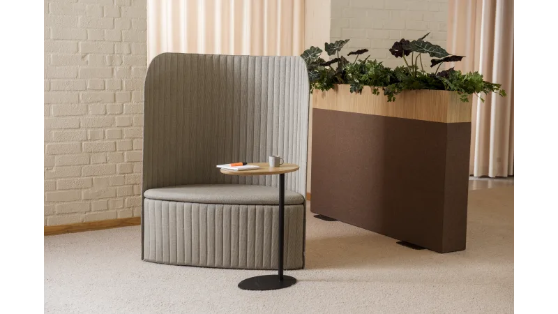 High-back acoustic lounge chair with a small side table beside a large office planter filled with greenery.