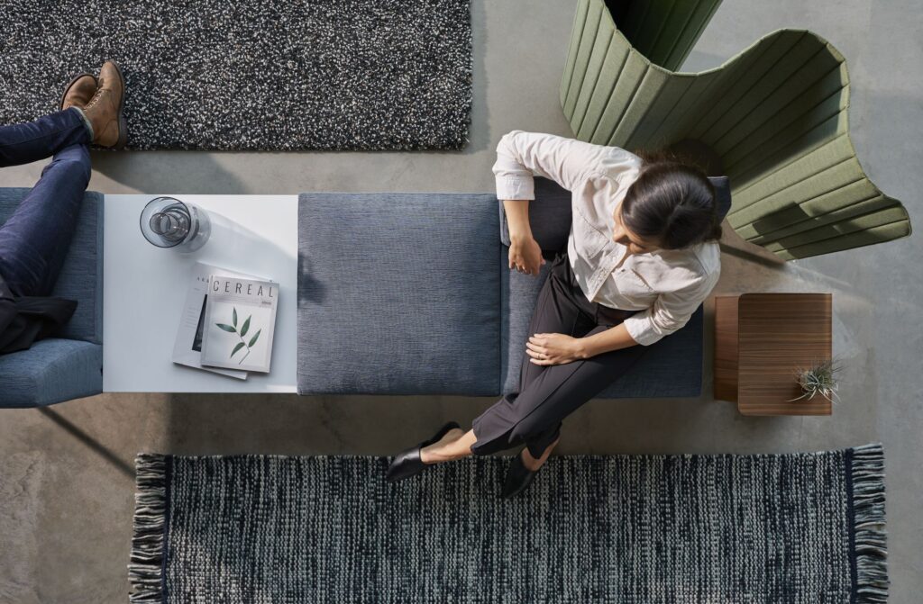 Overhead view of professionals seated on modular office lounge furniture with side tables, rugs, and a privacy chair.