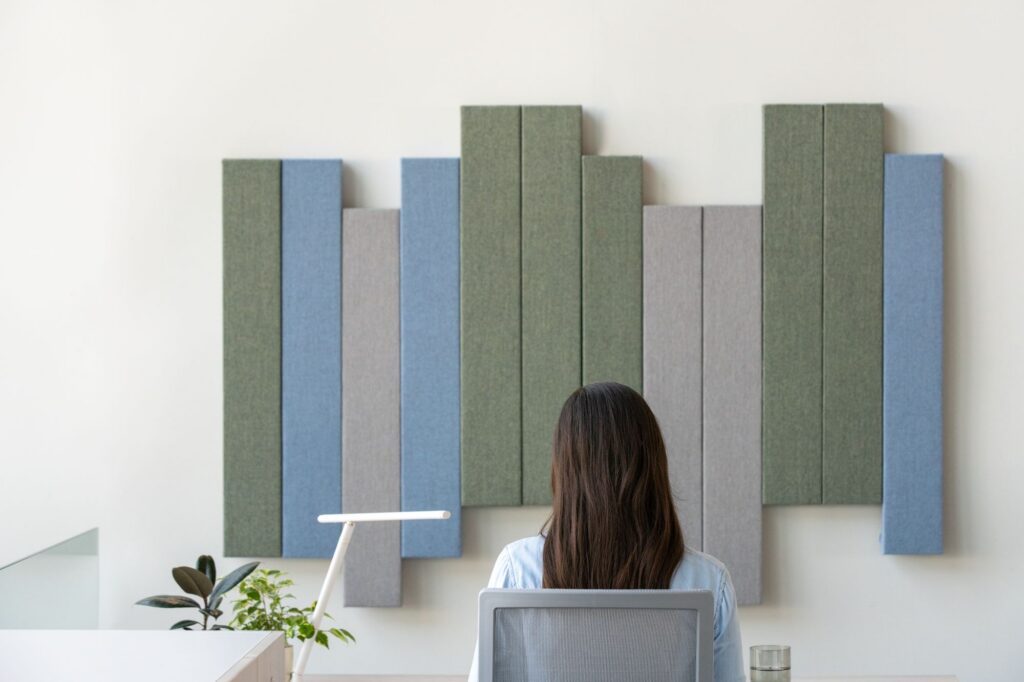 Employee seated at a modern workstation beneath decorative fabric acoustic wall panels in green, blue, and gray.