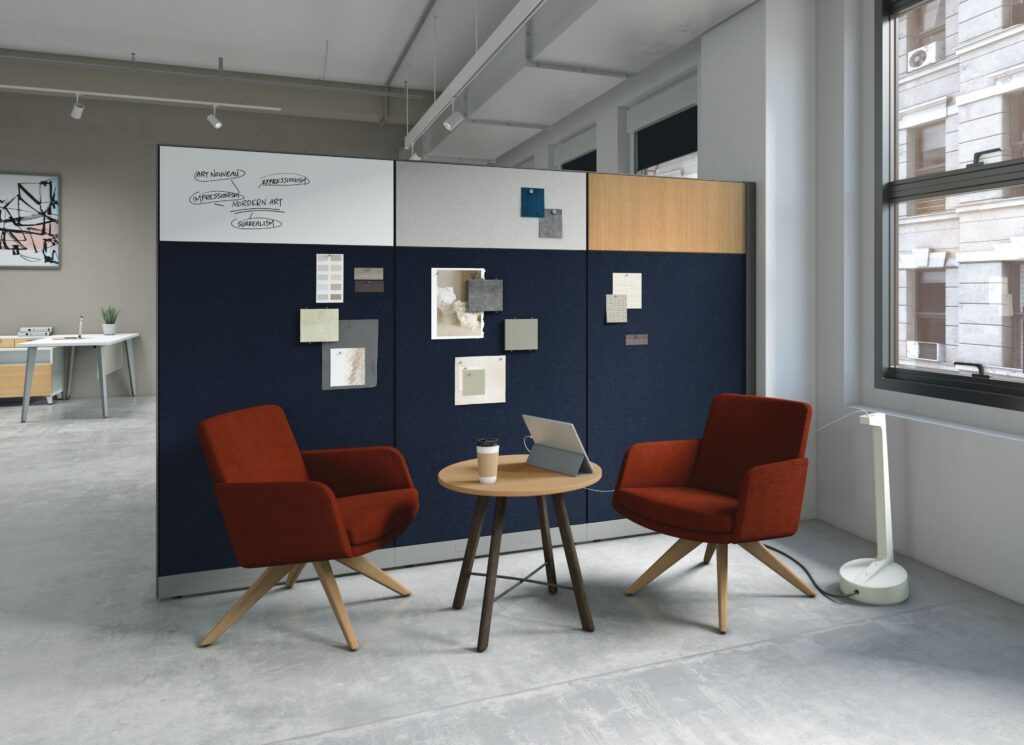 Informal office collaboration area with two lounge chairs, a round table, tablet, floor lamp, and multifunction acoustic partition.