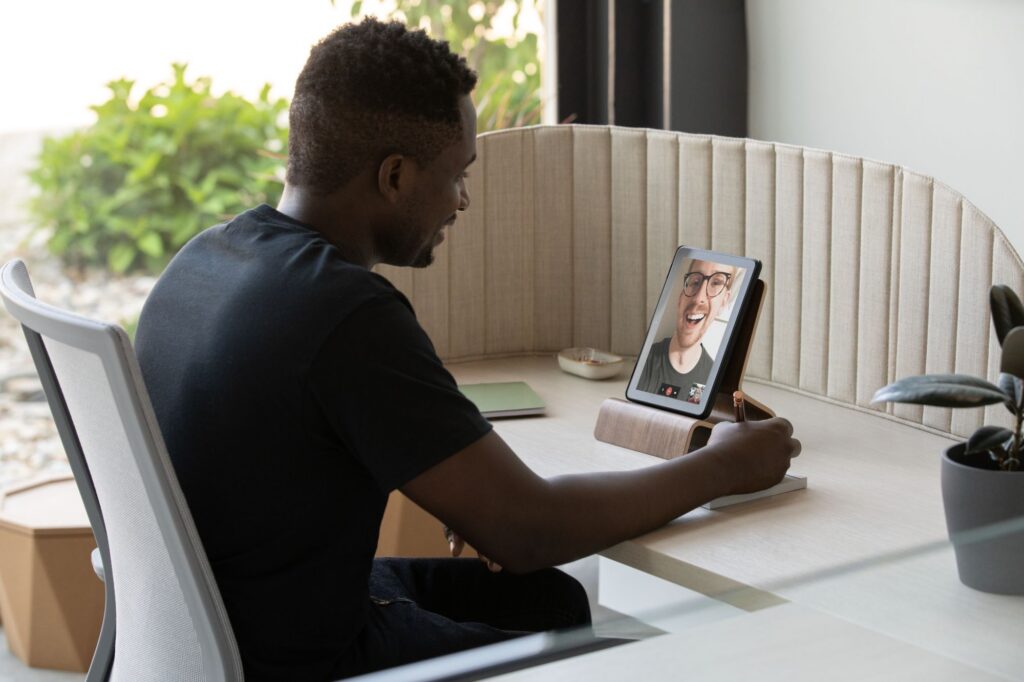 Professional participating in a video call on a tablet at a private workstation with an ergonomic chair and acoustic privacy screen.